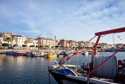 Sailboats moored in harbor by city against sky