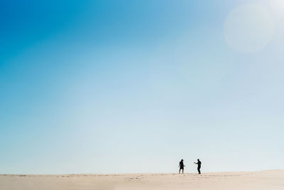 People on desert against clear blue sky