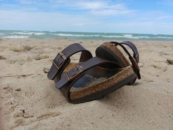 Abandoned shoes on sand at beach against sky