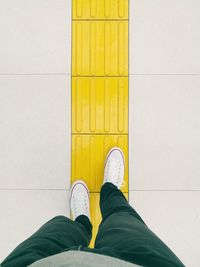 Low section of man standing against yellow wall