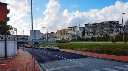 Road by buildings against sky in city