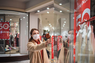 Happy woman wearing mask pointing at garment in store