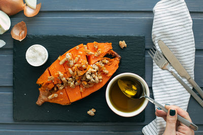 Baked sweet potato served on a slate board. female hand is pouring olive oil on the meal