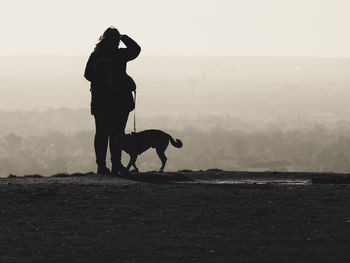 Silhouette man with dog on field against sky