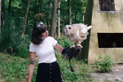 Woman looking at owl perching on her hand in forest