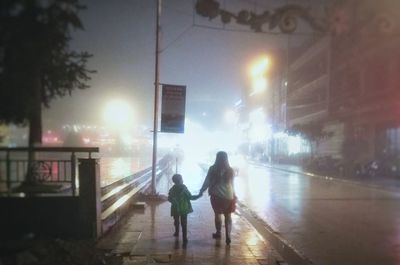 Rear view of people walking on street at night