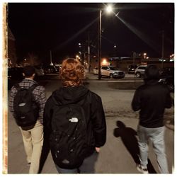 Rear view of man standing on city street at night