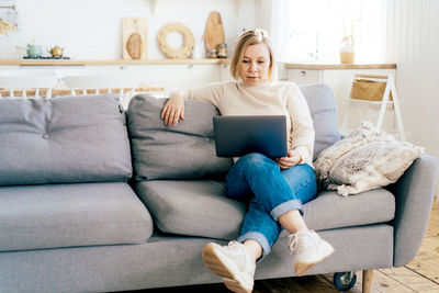 Full length of woman using laptop while sitting on sofa at home