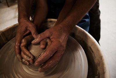 Cropped hands of man assisting child while making pot in workshop