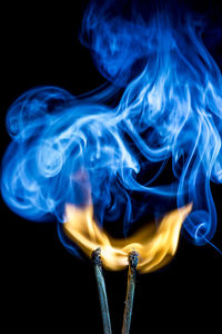 Close-up of burning matchstick with smoke against black background