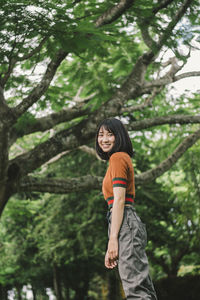 Side view of smiling young woman standing in forest