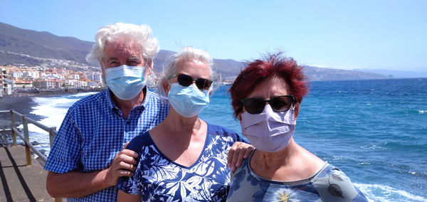 Portrait of friends wearing mask at beach against sky