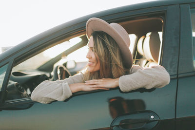 Smiling woman looking through window while sitting in car