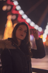 Portrait of young woman standing against illuminated wall
