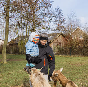 Mature man with granddaughter looking at goats on field