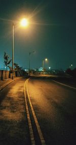 Empty road along illuminated street lights in city at night