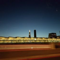 Light trails on bridge in city against clear sky at night