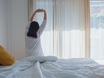 Rear view of woman relaxing on bed at home