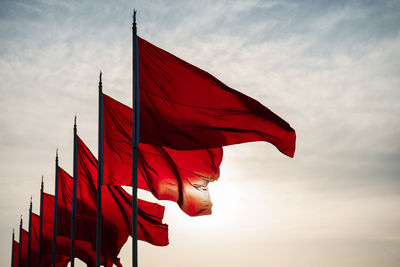 Low angle view of red flags waving in row against sky during sunset