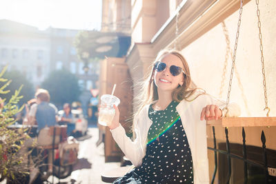 Young woman wearing sunglasses standing against buildings in city