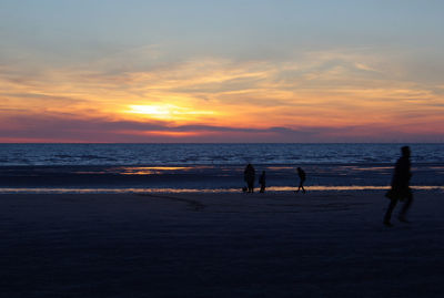 Silhouette people on beach against sky during sunset