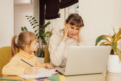 Working mom works from home office with kid. stressed woman using laptop.  woman freelancer