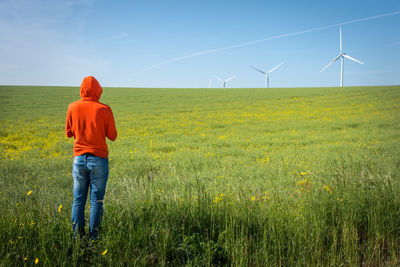 Rear view of man standing at farm against windmills