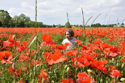 Young woman standing amidst yellow flowering plants on field against sky