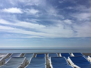 Row of chairs on beach against sky