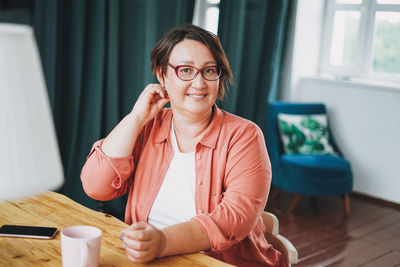 Adult charming brunette woman in glasses plus size body positive with cup of tea at home