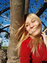 Portrait of smiling young woman against tree trunk