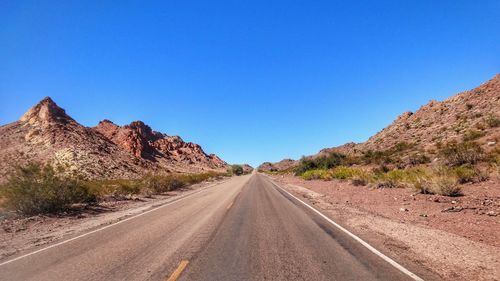 Road amidst desert against clear blue sky