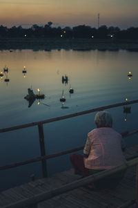 Rear view of men sitting on railing by lake