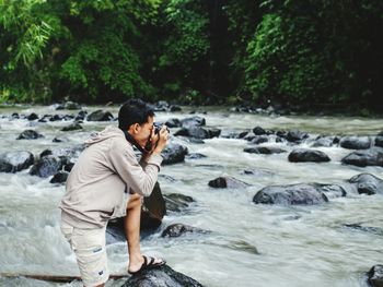 Full length of man standing on rock while photographing by river