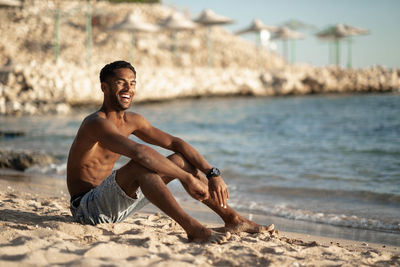 Side view of young man sitting at beach