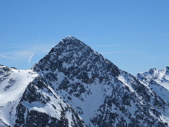 Low angle view of snowcapped mountains against clear blue sky