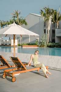 Woman sitting on lounge chair by swimming pool