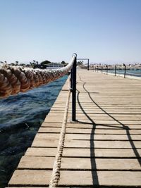 Wooden post on footpath by sea against clear sky