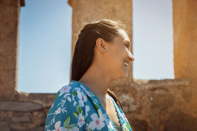 Side profile photo of a young woman in a summer dress enjoying warm sunlight