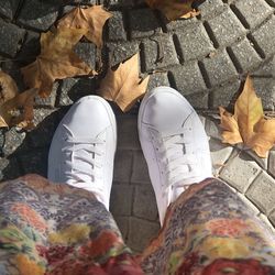 Low section of person wearing white shoes standing on footpath during autumn