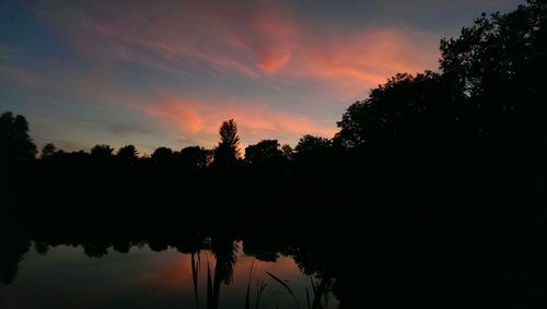 Reflection of silhouette trees in calm lake at sunset