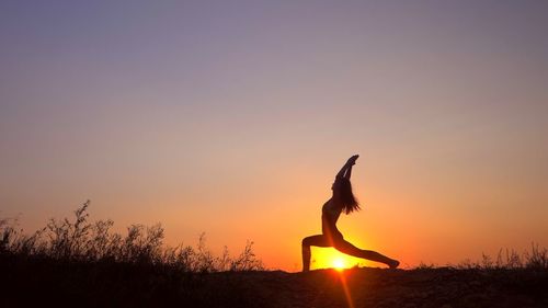 Woman practicing yoga on field against sky during sunset