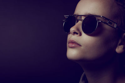 Close-up portrait of woman wearing sunglasses against black background