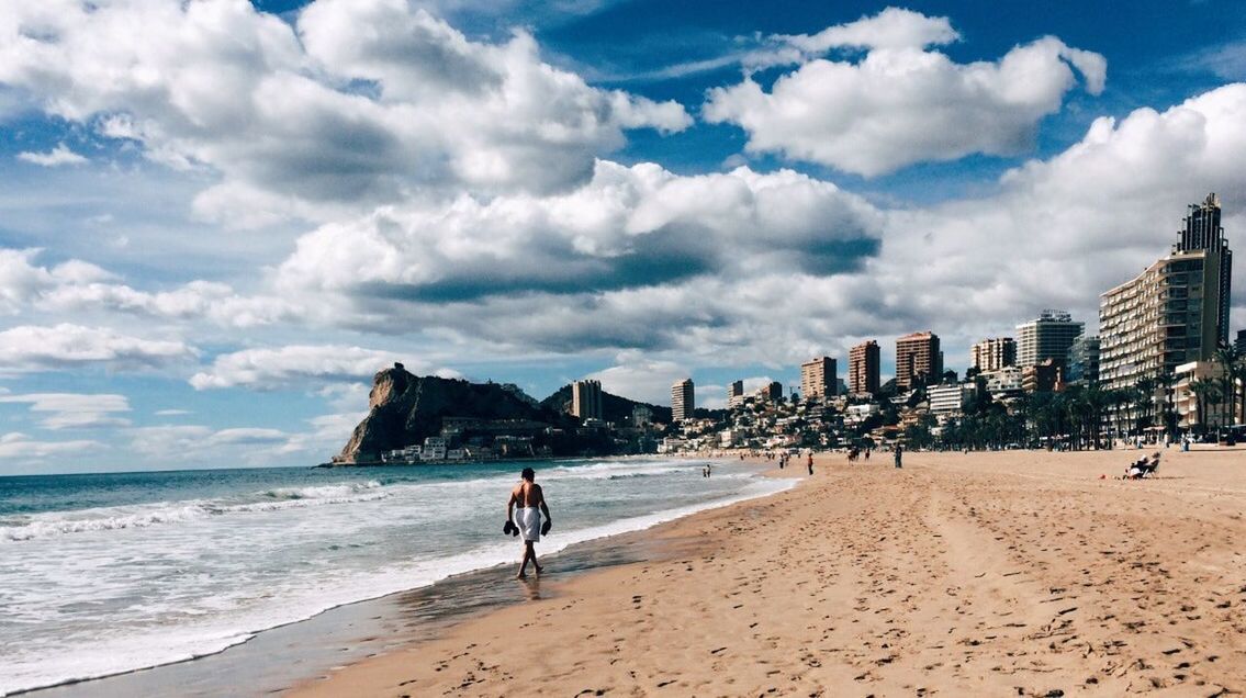 beach, sea, sand, sky, shore, water, lifestyles, leisure activity, cloud - sky, full length, walking, vacations, men, person, cloud, tourist, building exterior, built structure, coastline