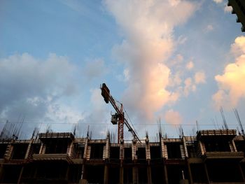 Low angle view of crane by building against sky