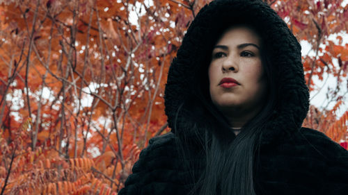 Portrait of young woman standing against trees