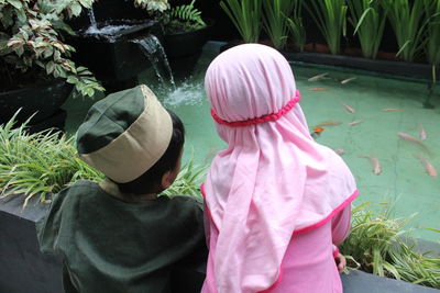 Rear view of children wearing traditional clothing looking at fishes swimming in artificial pool