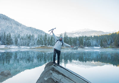 Portrait of smiling man standing with tripod on cliff against lake 