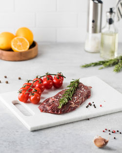 A piece of fresh raw beef steak on a board with rosamarin and cherry podimors.