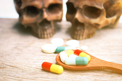 Close-up of wooden spoon with pills and human skulls on table